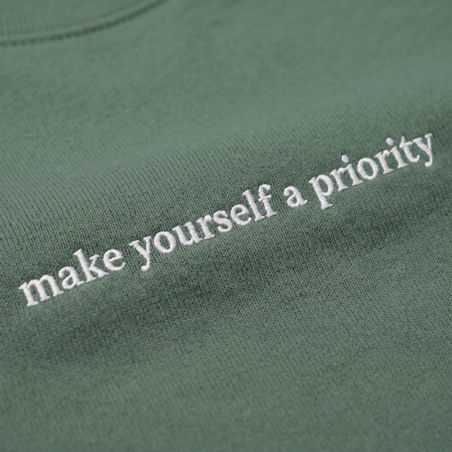 Moteriško džemperio su siuvinėtu užrašu „Make Yourself a Priority“ detalė
