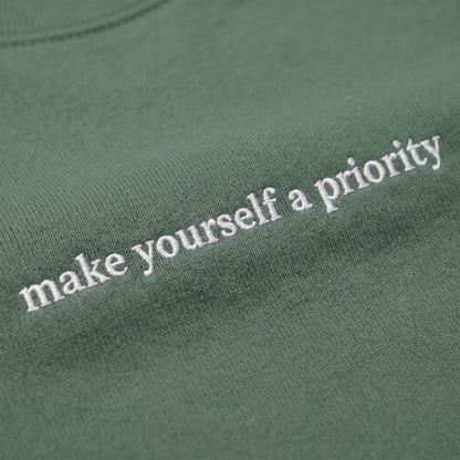 Moteriško džemperio su siuvinėtu užrašu „Make Yourself a Priority“ detalė
