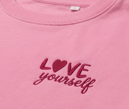 Siuvinėtas LOVE yourself užrašas ant rožinio džemperio