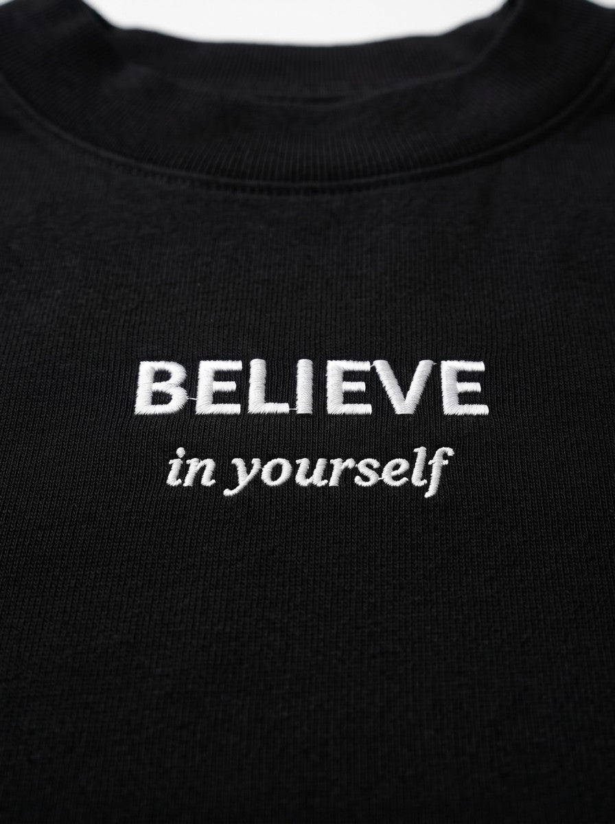 Kokybiško balto siuvinėjimo „BELIEVE in yourself“ detalė ant juodų moteriškų marškinėlių.