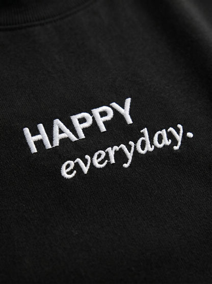 Kokybiško balto siuvinėjimo „HAPPY everyday.“ detalė ant juodų moteriškų marškinėlių.