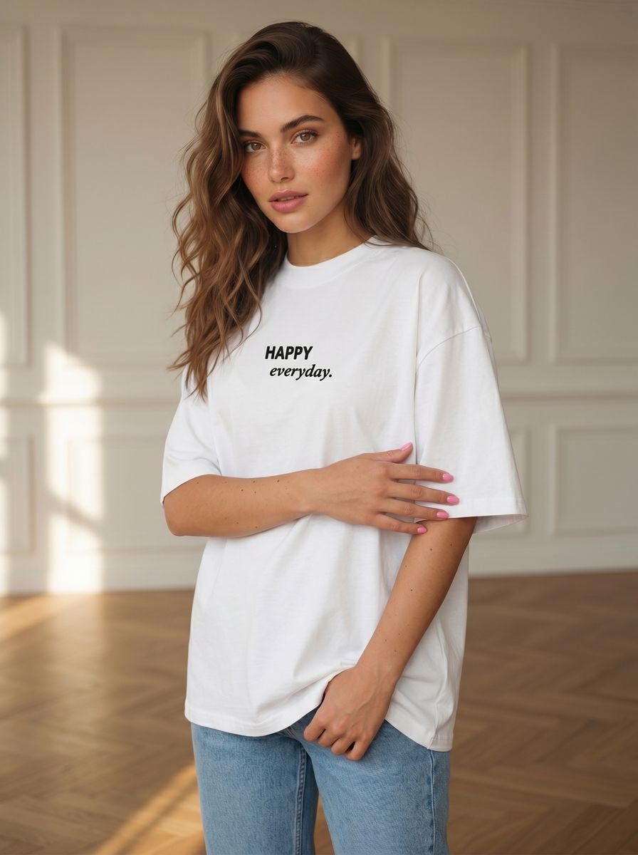 Balti oversize marškinėliai moterims su juodu siuvinėtu užrašu „HAPPY everyday.“ ant modelio studijoje.