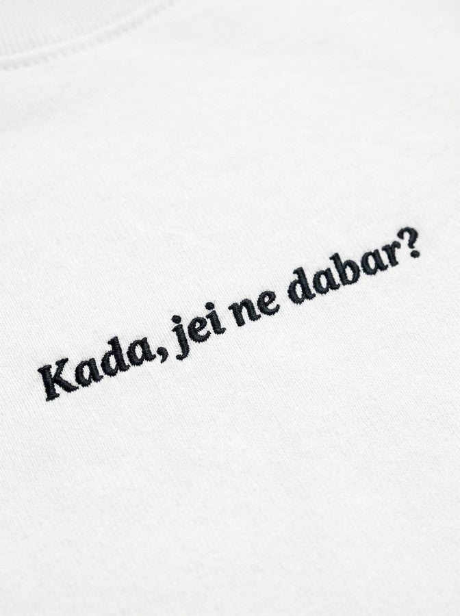 Kokybiško juodo siuvinėjimo „Kada, jei ne dabar?“ detalė ant baltų moteriškų marškinėlių audinio.